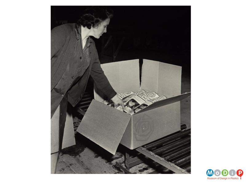 Scanned image showing a female worker packing bags of roses into a box.