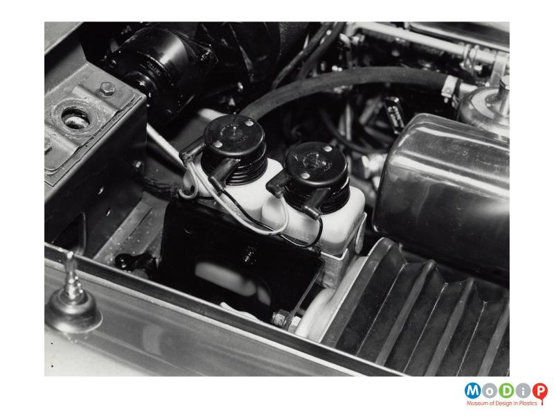 Scanned image showing two fluid containers in the engine bay of a car.