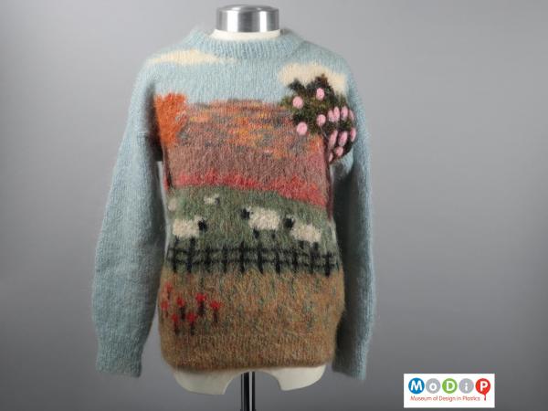 Front view of a jumper showing the multicoloured sceen with fence, sheep, and trees.