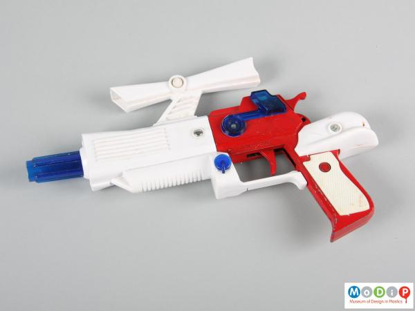 Side view of a toy gun showingthe red metal handle and white and blue plastic attachments.