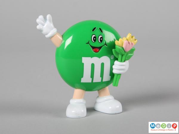 Front view of a green M&M figure showing the smiling face, flowers, and limbs.