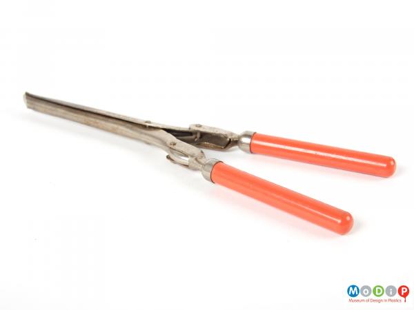 Side view of a pair of folding hair tongs showing the orange handles extended.