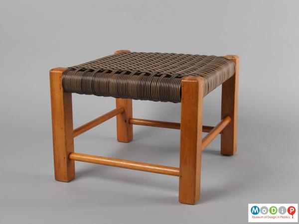 Side view of a footstool showing the wooden frame and woven seat.