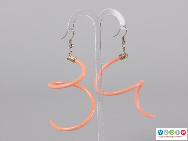 Side view of a pair of earrings made from knitting needles hanging on a stand.