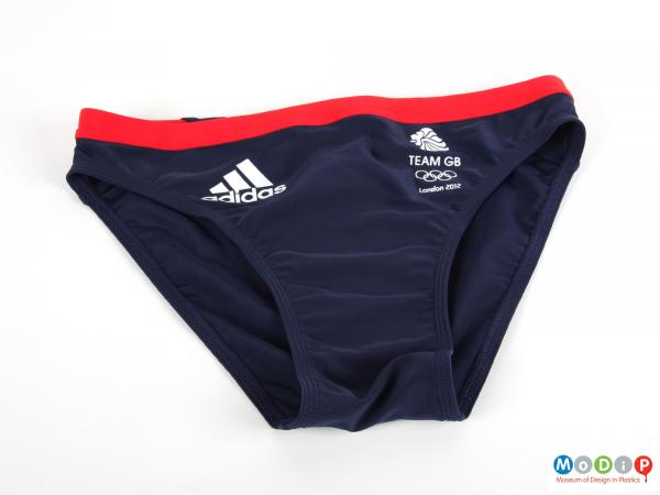 Front view of a pair of swimming trunks showing the red waist band and white printed logos.