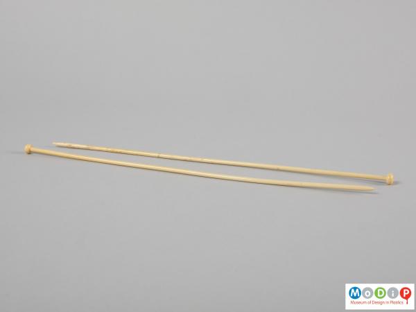 Side view of a pair of knitting needles showing a curve in the profile.