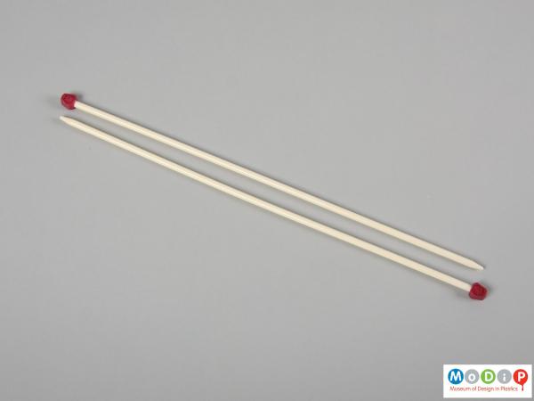 Side view of a pair of knitting needles showing the plain shaft and coloured head.