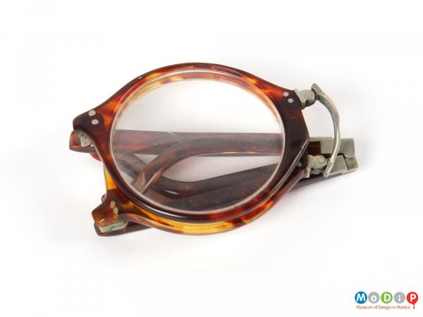 Front view of a pair of folding glasses showing the lenses and arms folded to their minimum size.