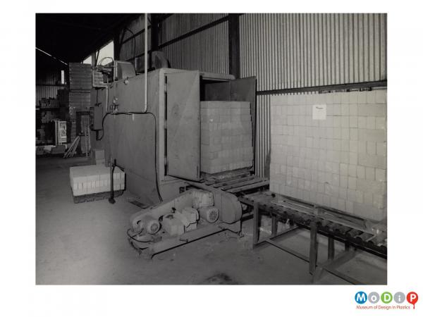 Scanned image showing pallet loads of bricks going though a machine which heats and shrinks the wrapping.