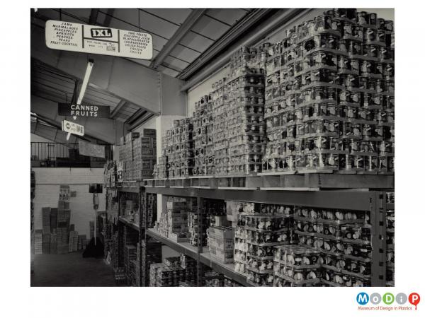 Scanned image showing a warehouse full of shrink wrapped crates of tinned fruit.
