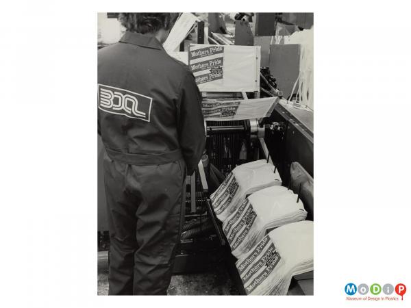 Scanned image showing a male working operating a machine sorting bread bags.