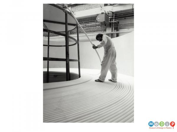 Scanned image showing a male worker placing coils of cable into a storage container.