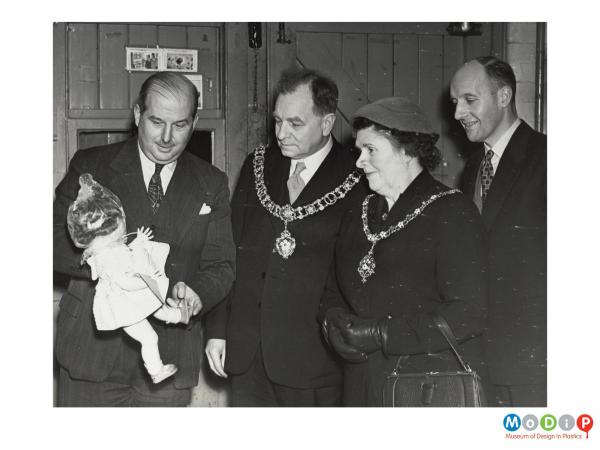 Scanned image showing a Mayoral group looking at a doll.