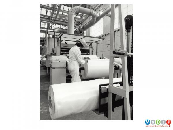Scanned image showing a male worker by rolls of sheeting.