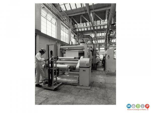 Scanned image showing a male worker at a machine producing rolls of sheeting.