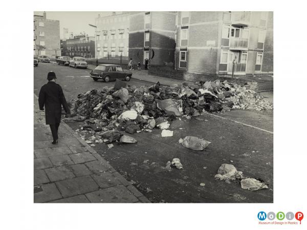 Scanned image showing a street scene depicting piles of filled rubbish bags.