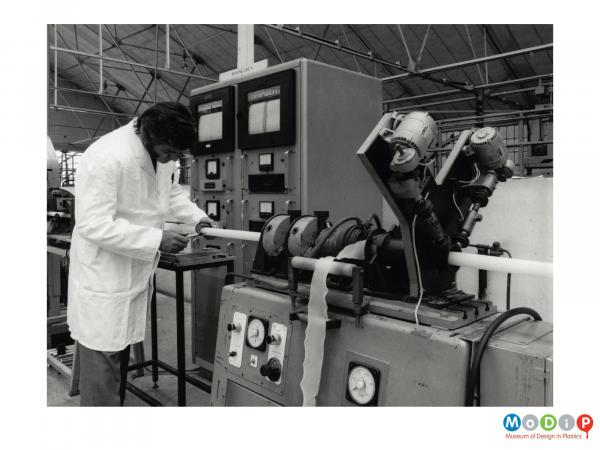 Scanned image showing a man measuring an extrude tube.