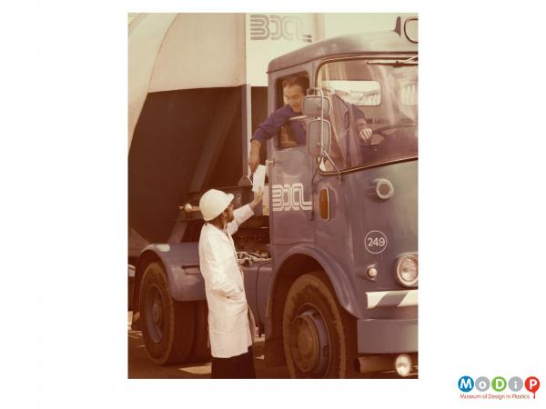 Scanned image showing a man driving a tanker taking a certificate from another man.