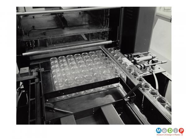 Scanned image showing a machine gathering empty jars in order to shrink wrap them.