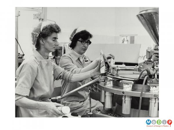 Scanned image showing two women removing filled tubes from a sealing machine.