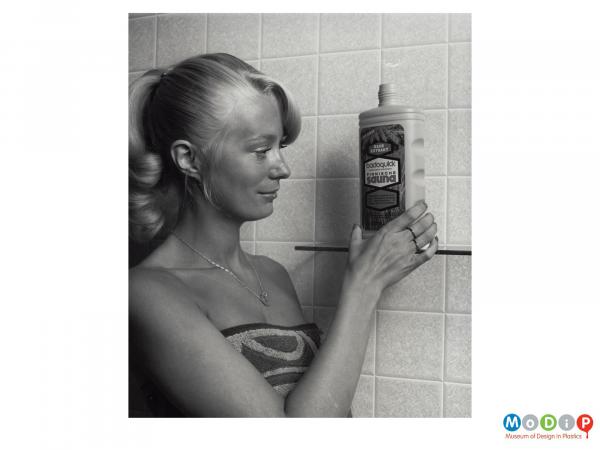 Scanned image showing a woman wearing a towel and looking at a bottle on a shelf.