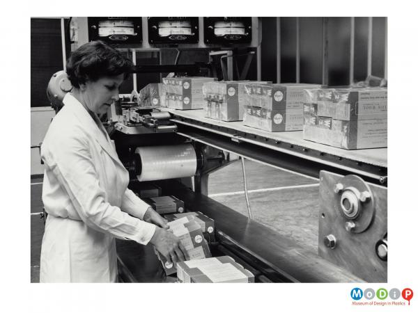 Scanned image showing a woman packing boxes in a shrink wrapping machine.