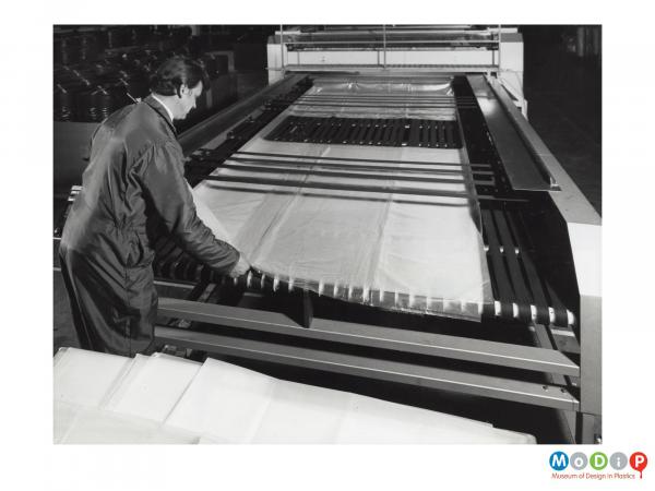 Scanned image showing a man at a bag making machine.