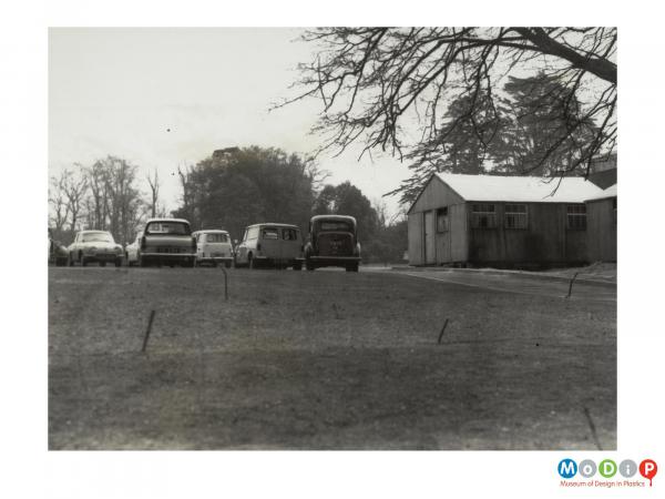 Scanned image showing cars parked by an outbuilding.