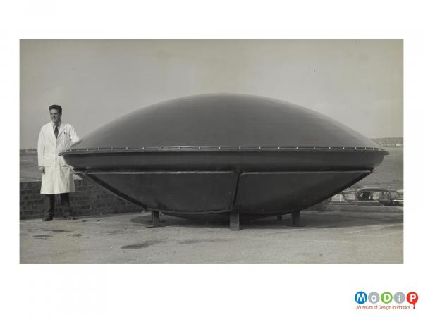 Scanned image showing a man standing next to a dish shaped aerial.