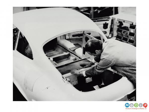 Scanned image showing  male worker fitting a Plastazote panel into the back of an E-type jag.