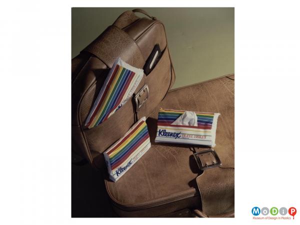 Scanned image showing three packets of travel tissues along with two suitcases.
