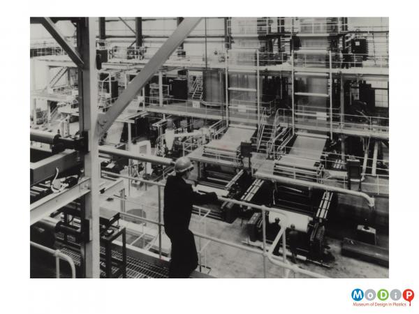 Scanned image showing a man looking down onto a factory floor.