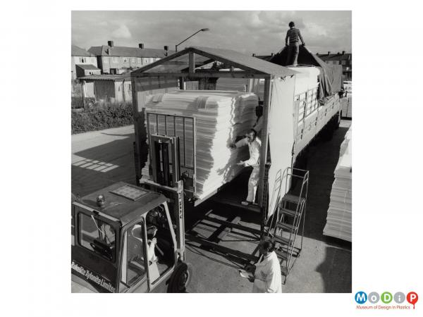 Scanned image showing stacks of material being loaded onto a lorry.