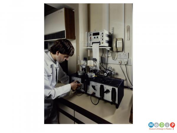 Scanned image showing a male in a white coat measuring materials in a laboratory.