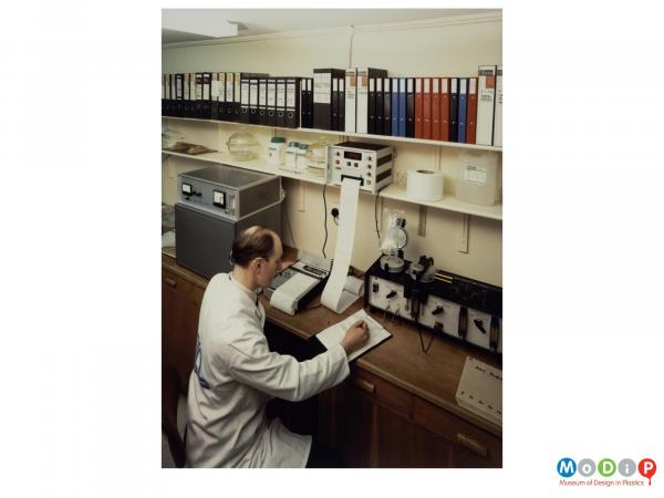 Scanned image showing a man in a white coat taking readings in a laboratory.