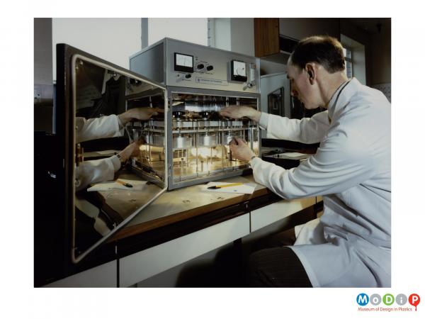 Scanned image showing a man in a white coat using a scientific device.