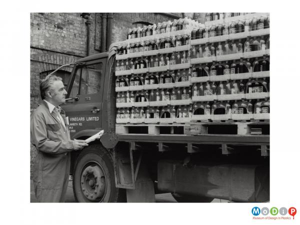 Scanned image showing a man checking a lorry load of shrink wrapped bottles.