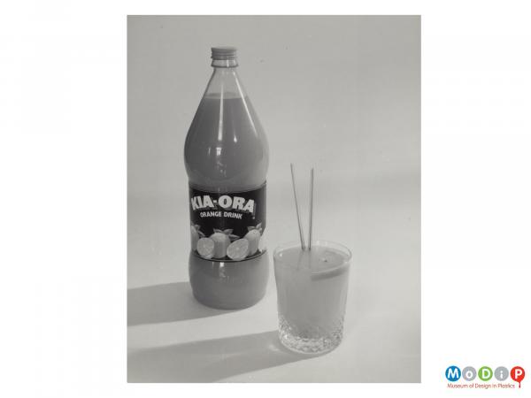 Scanned image showing a bottle of Kia-Ora orange drink along side a tumbler with 2 straws.