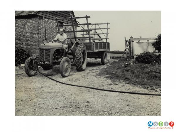 Scanned image showing a man driving a tractor and cart over a pipe.