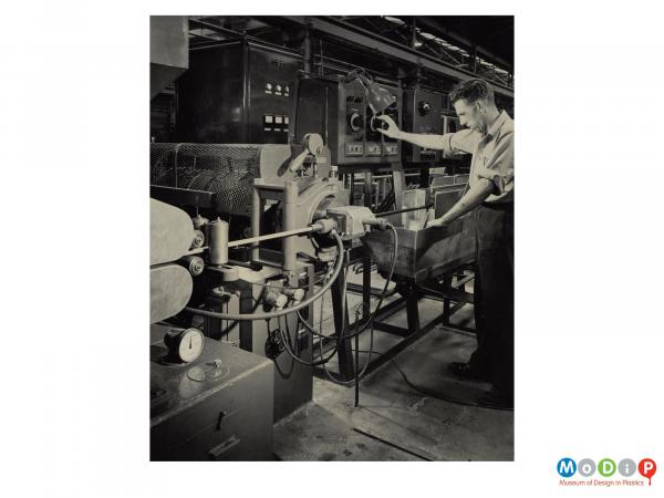 Scanned image showing a male worker at an extruding machine.