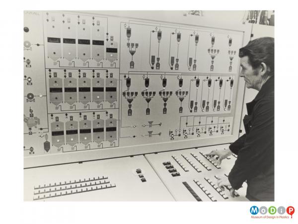 Scanned image showing a male worker standing at a control panel.