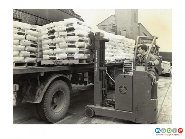 Scanned image showing sacks of raw plastics being loaded onto a truck.