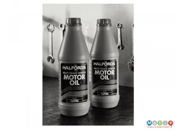 Scanned image showing two bottles of motor oil in front of a several spanners hanging on a wall.