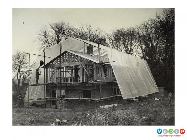 Scanned image showing a house being protected by sheet plastic during building.