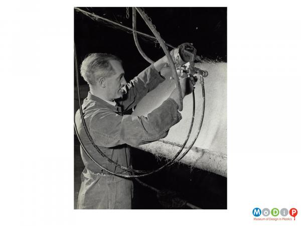 Scanned image showing a man spraying glass fibres and resin into a mould.