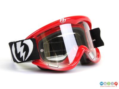 Side view of a pair of Electric goggles showing the clear lenses and red frames.