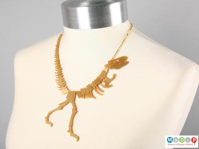 Front view of a Tatty Devine necklace showing the shape of the dinosaur on the neck of a mannequin.