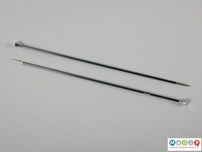 Side view of a pair of knitting needles showing the plain shaft and metalised tip and head.